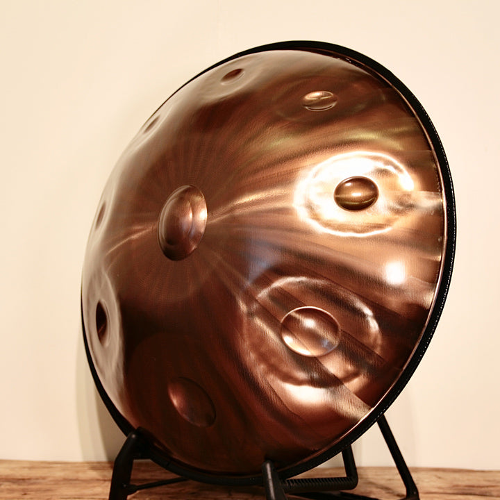 AeloPan Handpan Bronze glänzend steht auf einem Ständer vor weißer Wand. Man sieht die Handpan leicht gedreht von der Seite