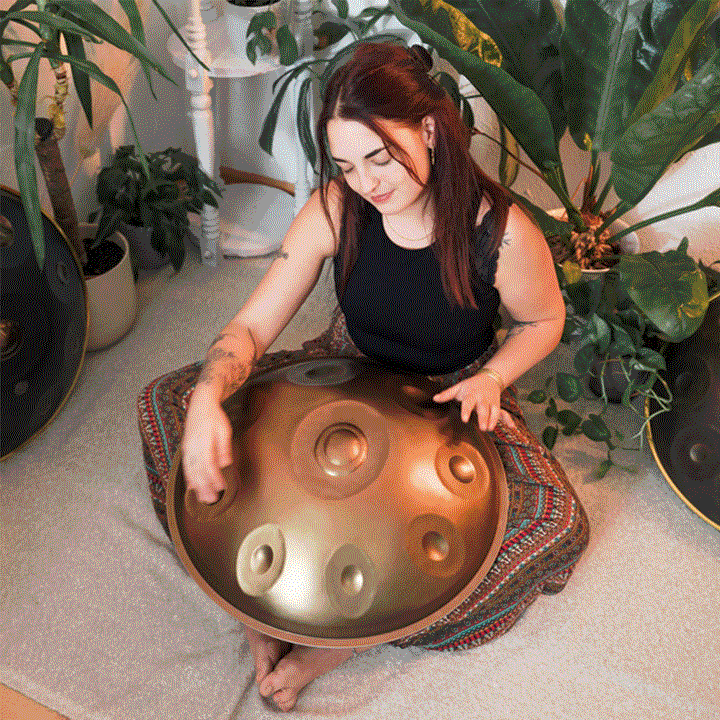 Versierte Handpanspielerin sitzt auf dem Boden in einem gemütlich eingerichteten Raum und spielt auf einer Nala Handpan