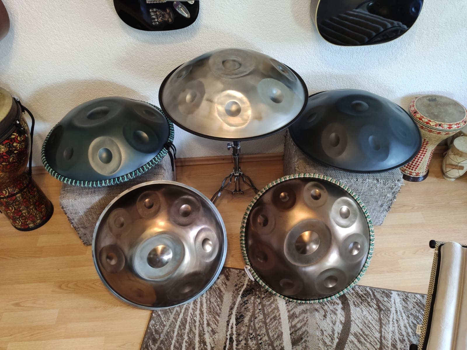 Mittig steht eine Handpan auf einem Ständer, links und rechts von ihr jeweils eine auf einem Hocker und davor lehnen zwei weitere.