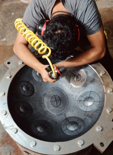 Zu sehen ist Abhinav, der Hersteller der Svaraa Handpans. Er formt die Oberseite einer Handpan Drum mit einem Druckluft-Hammer. 