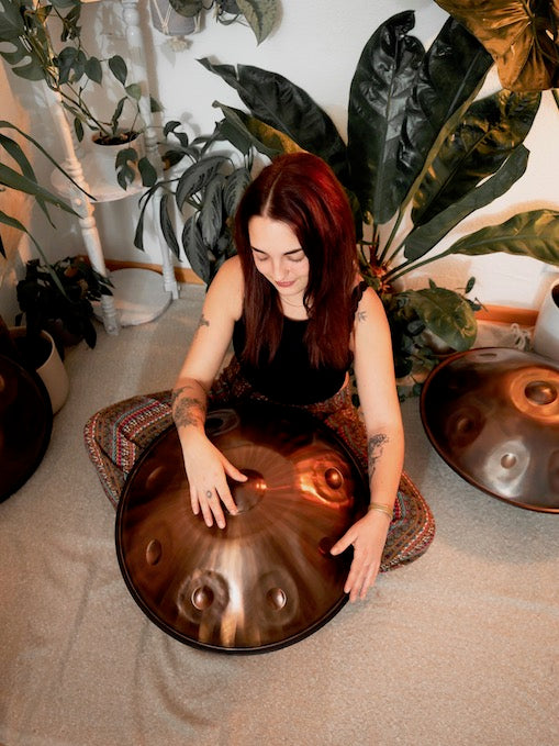 Schöne Handpan Musikerin aus Freiburg sitzt auf dem Boden, vor ihr liegt eine Edelstahl Handpan in 440 Hz auf einem Ständer