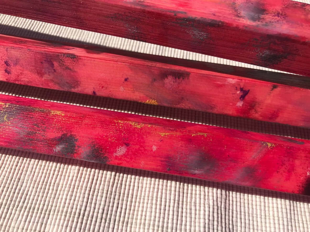 Nahaufnahme des rot-angemalten Holz-Handpan-Ständers mit schwarz grauen Details. Er liegt auf einem Holztisch