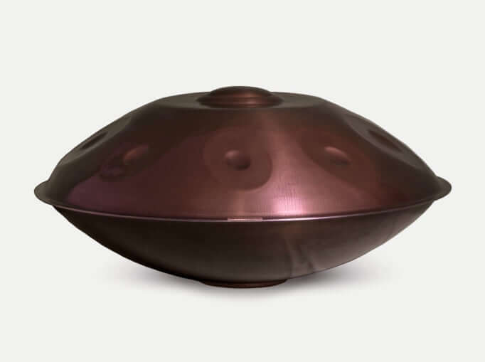 Eine Healing Frequency Handpan F2 Low Pygmy in einem bronzefarbenen Edelstahl mit rötlichen Schimmer und 9 sichtbaren Tonfeldern auf weißen Hintergrund.