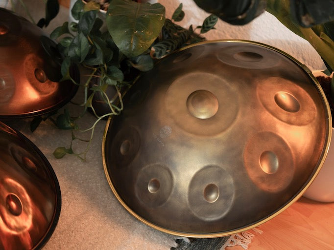 Handgefertigte KitaPantam Handpan in dem Design Gold Vintage liegt zwischen anderen Handpans und Pflanzen auf dem Boden
