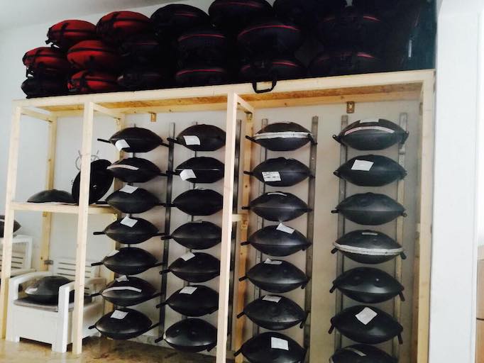 28 gerade hergestellte Black Magic Handpans liegen bei dem Hersteller im Regal. Oben Drauf liegen viele Evatec Hardcases in rot und schwarz.