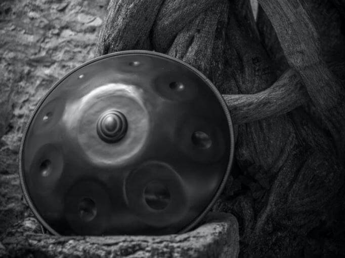 Ein schwarz-weiß Bild einer nitrierten Handpan, welche auf einen Stein gestellt und an einen Baum gelehnt wurde. 